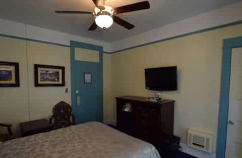 Room painted in yellow and bright blue with a queen bed and ceiling fan.