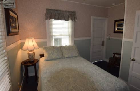 Queen bed in a bedroom with a ceiling fan and windows with blinds and valances.