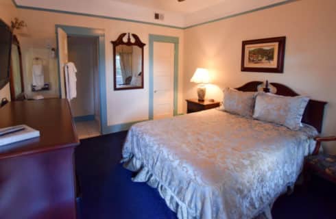 Bedroom painted white with blue trim holds a queen bed with a satin cover