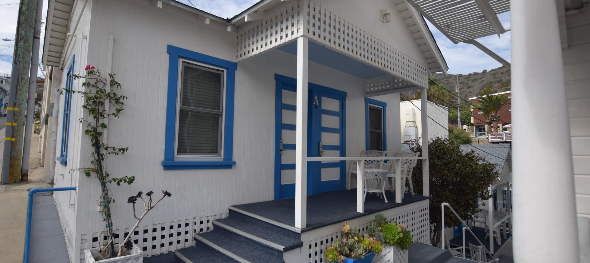 Quaint little cottage painted white with blue trim with a small front porch.