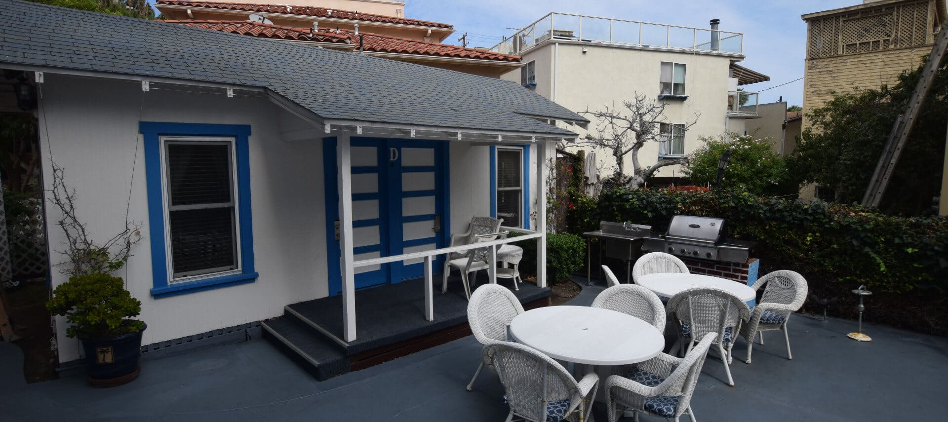 Cute little cottage painted white with blue trim with a small front porch and patio tables and chairs.