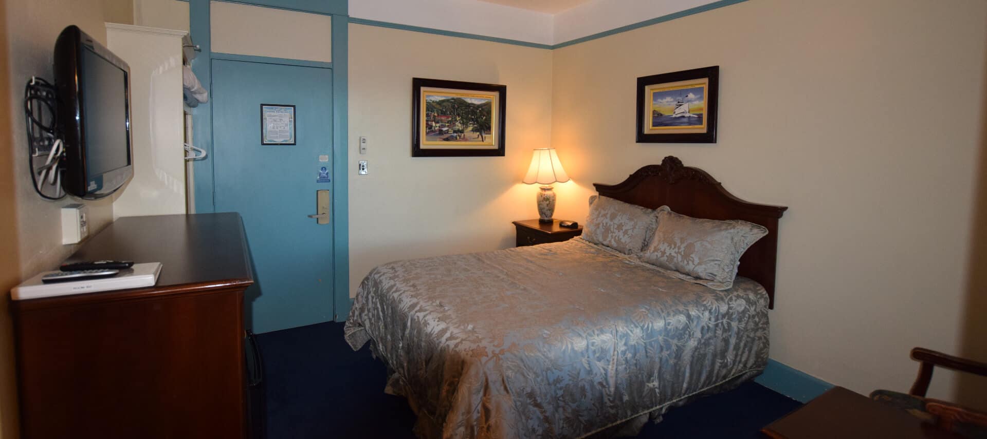 Room painted in pale yellow with blur trim holds a queen bed and a ceiling fan.