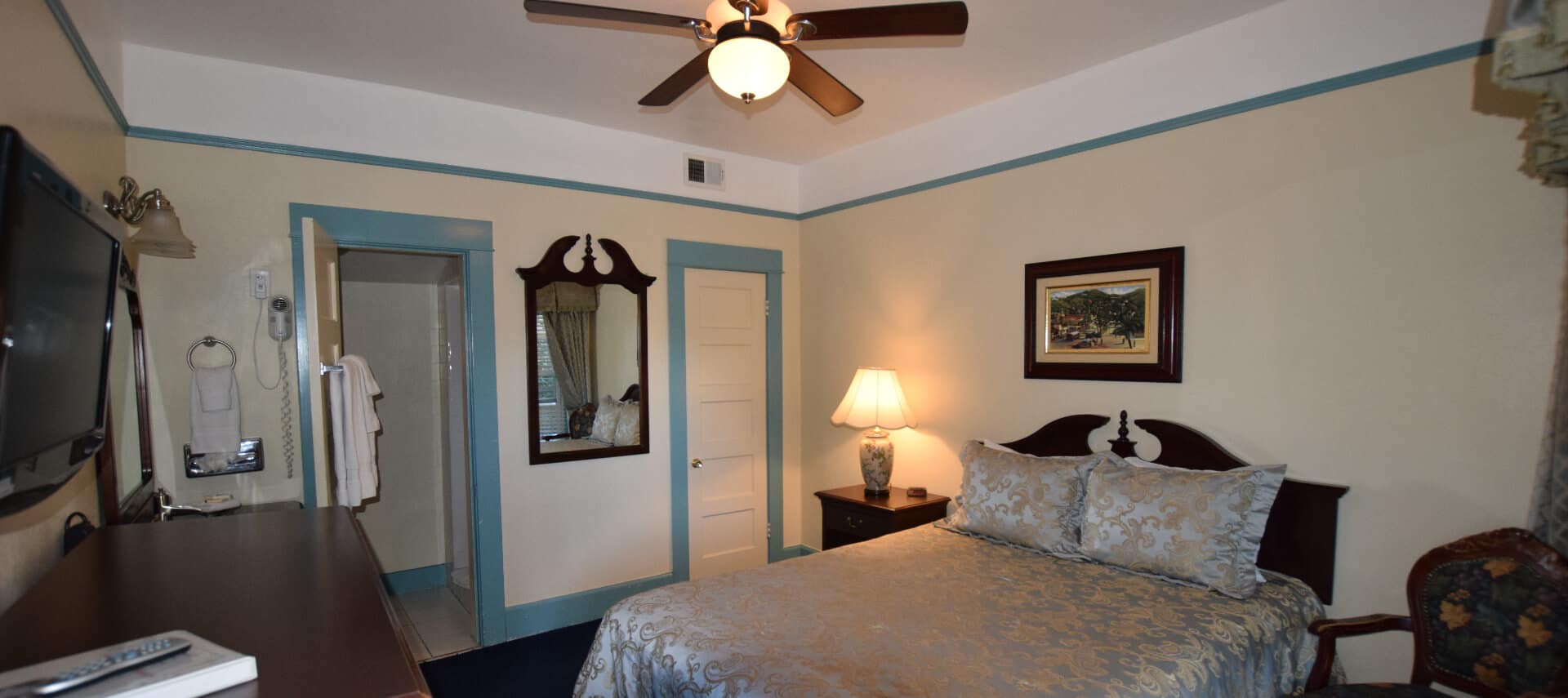 Bedroom painted white with blue trim holds a queen bed with a satin cover